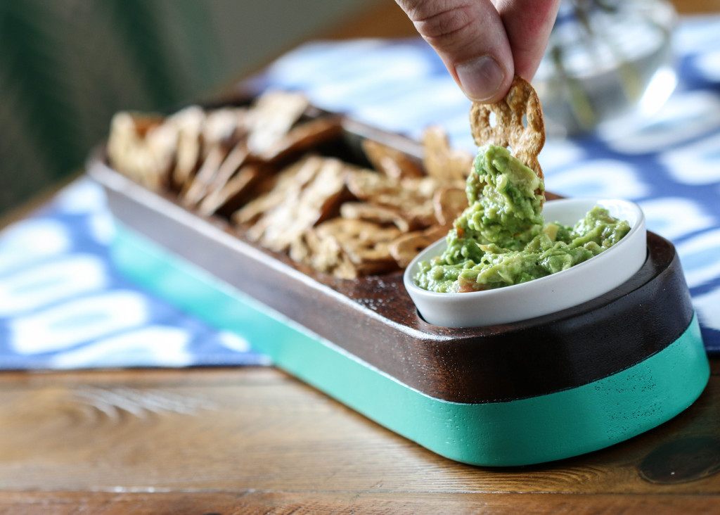 A hand dipping a cracker into a bowl of guacamole