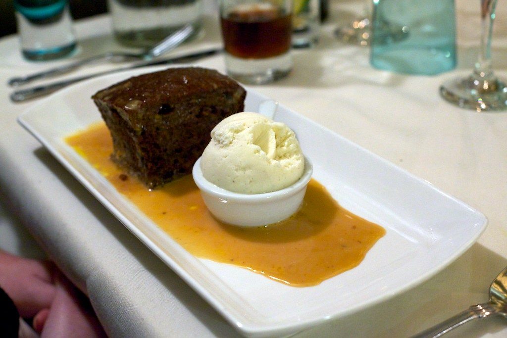 A steamed pudding in a pool of sauce with ice cream